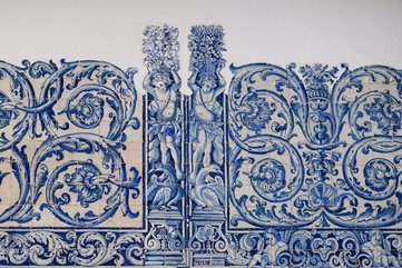 Painel de azulejos portugueses em tons de azul, com figuras humanas estilizadas segurando cestos de flores e motivos florais ornamentais ao redor.