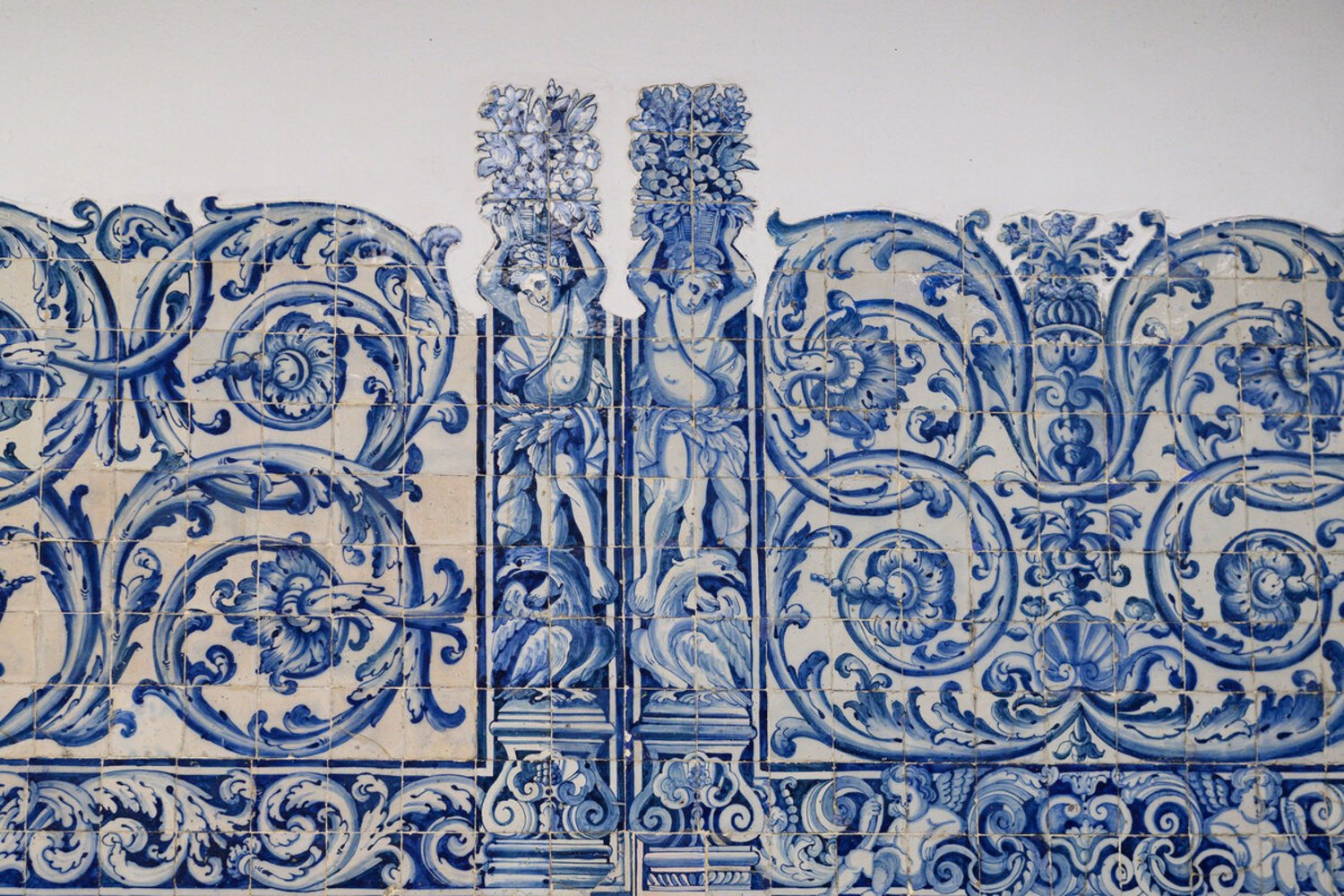 Painel de azulejos portugueses em tons de azul, com figuras humanas estilizadas segurando cestos de flores e motivos florais ornamentais ao redor.